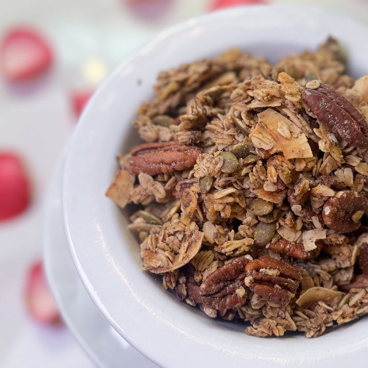 White container filled with granola on a surface with pink petals