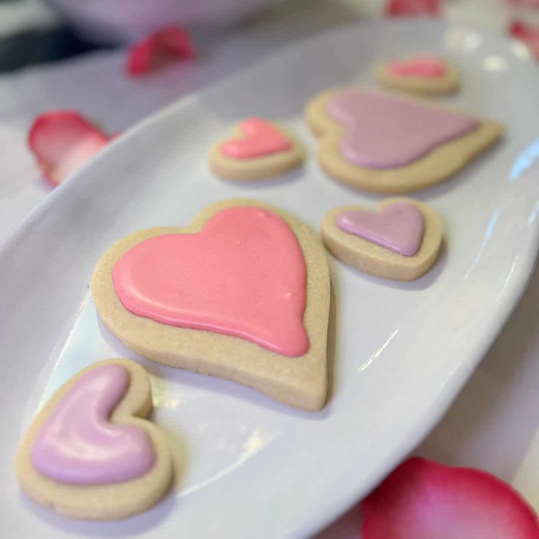 Heart-shaped cookies with pink and purple icing on a white plate.