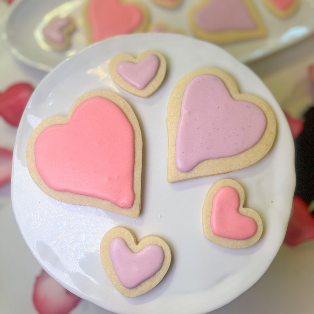 Heart-shaped cookies with pink and white icing on a white plate.